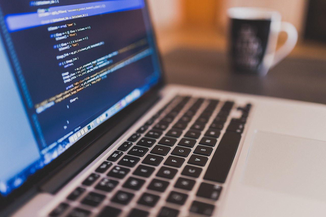 A laptop displaying code in an editor beside a coffee mug on a desk.