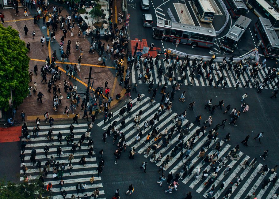 An aerial view of a large city intersection, several hundred pedestrians crossing at once over multiple diagonal crosswalks while buses wait along the top of the frame. Every person in that frame is taking a different route at a different speed, and that is precisely what field data is: not one measurement, but a distribution of them.