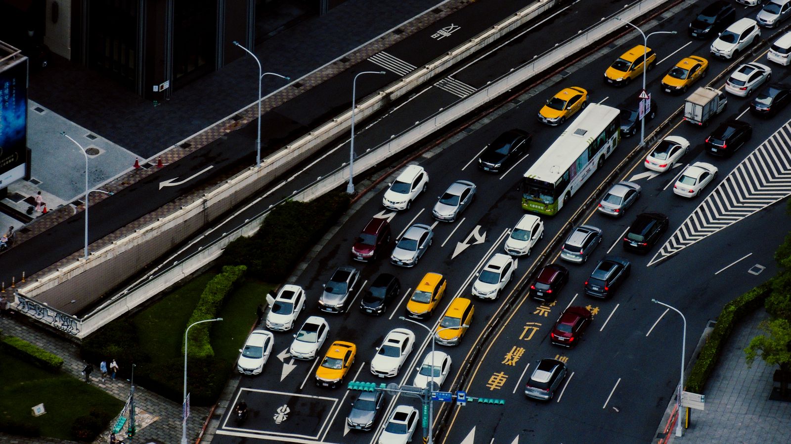 A city interchange seen from above: four lanes of cars, taxis and a bus completely stopped in queue on the right, while the two elevated lanes on the left carry no traffic at all.