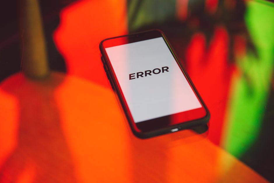 Ein Smartphone liegt auf einer Glasfläche, sein weißer Bildschirm zeigt nur das Wort ERROR in schwarzen Großbuchstaben, umgeben von roten, orangefarbenen und grünen Spiegelungen