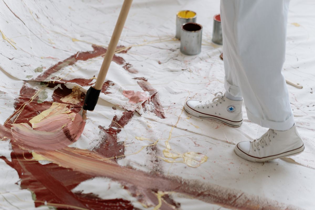 Eine große Leinwand flach auf dem Boden, ein langstieliger Pinsel verteilt dunkelrote Farbe darauf, daneben offene Farbdosen und eine Person in weißer Hose und weißen Turnschuhen am Rand. Die Leinwand füllt sich nach und nach, und genau das misst der Speed Index: nicht den Moment, in dem etwas erscheint, sondern wie sich die Fläche über die Zeit füllt.