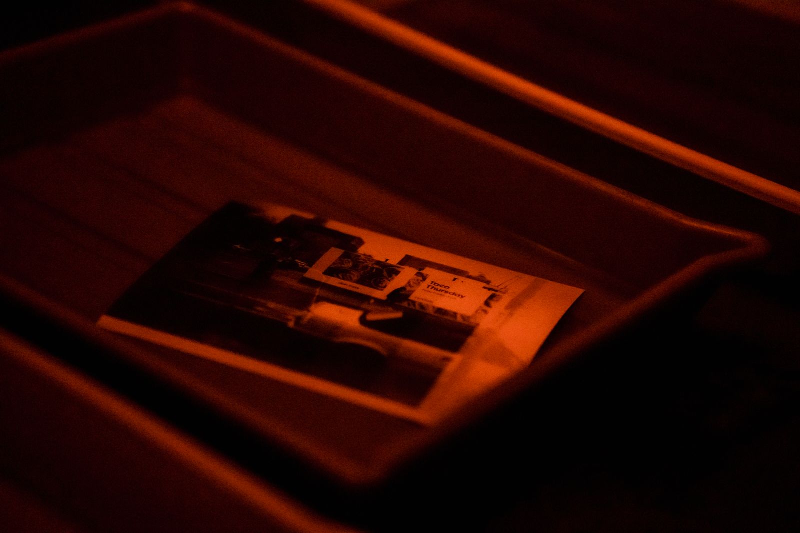 Ein fotografischer Abzug in einer Entwicklerschale unter rotem Dunkelkammerlicht, sein Bild teilweise sichtbar