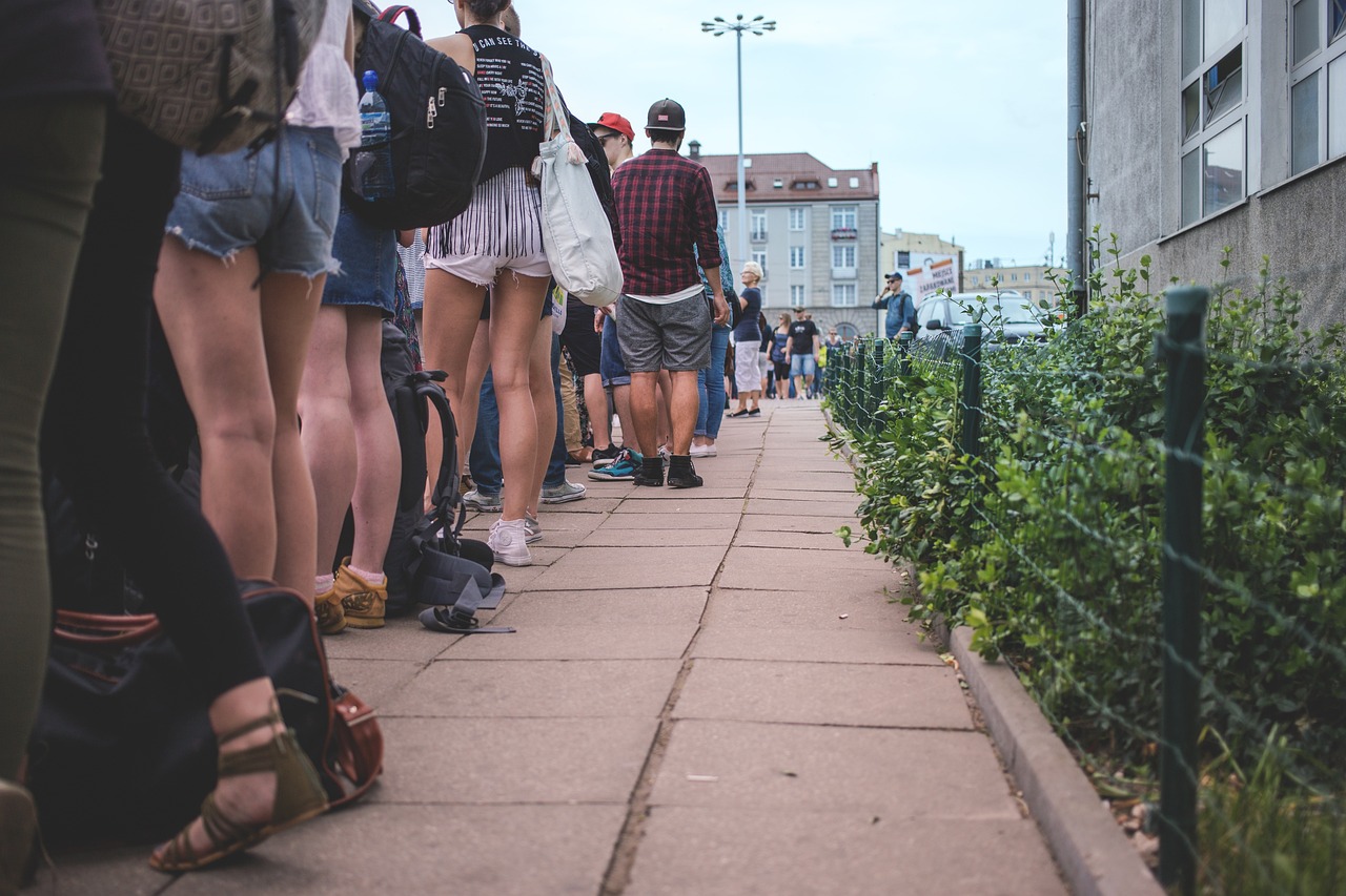A long queue of people waiting on a pavement, photographed at low angle along the line