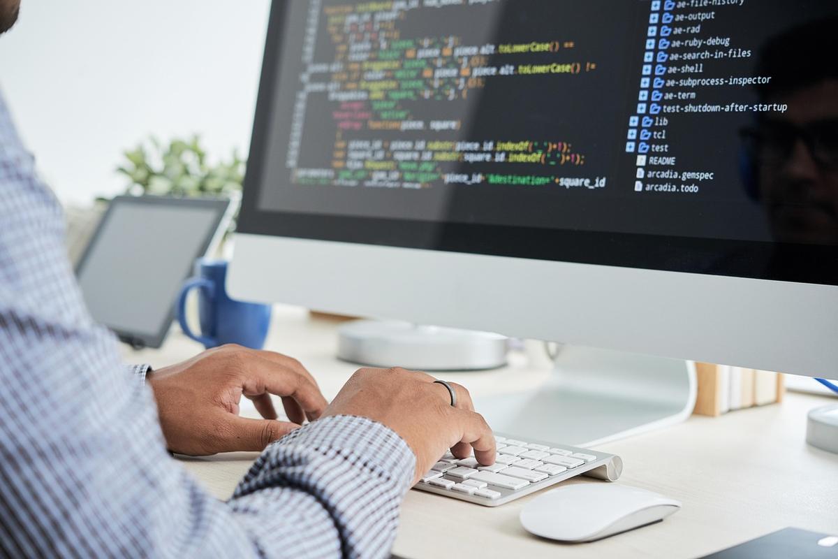 A developer typing code at a desktop computer showing a code editor.