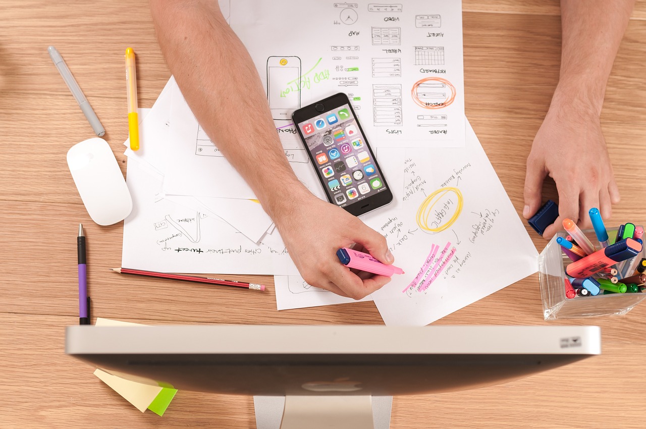 A top-down view of a UI design workspace with wireframe sketches, markers and a phone